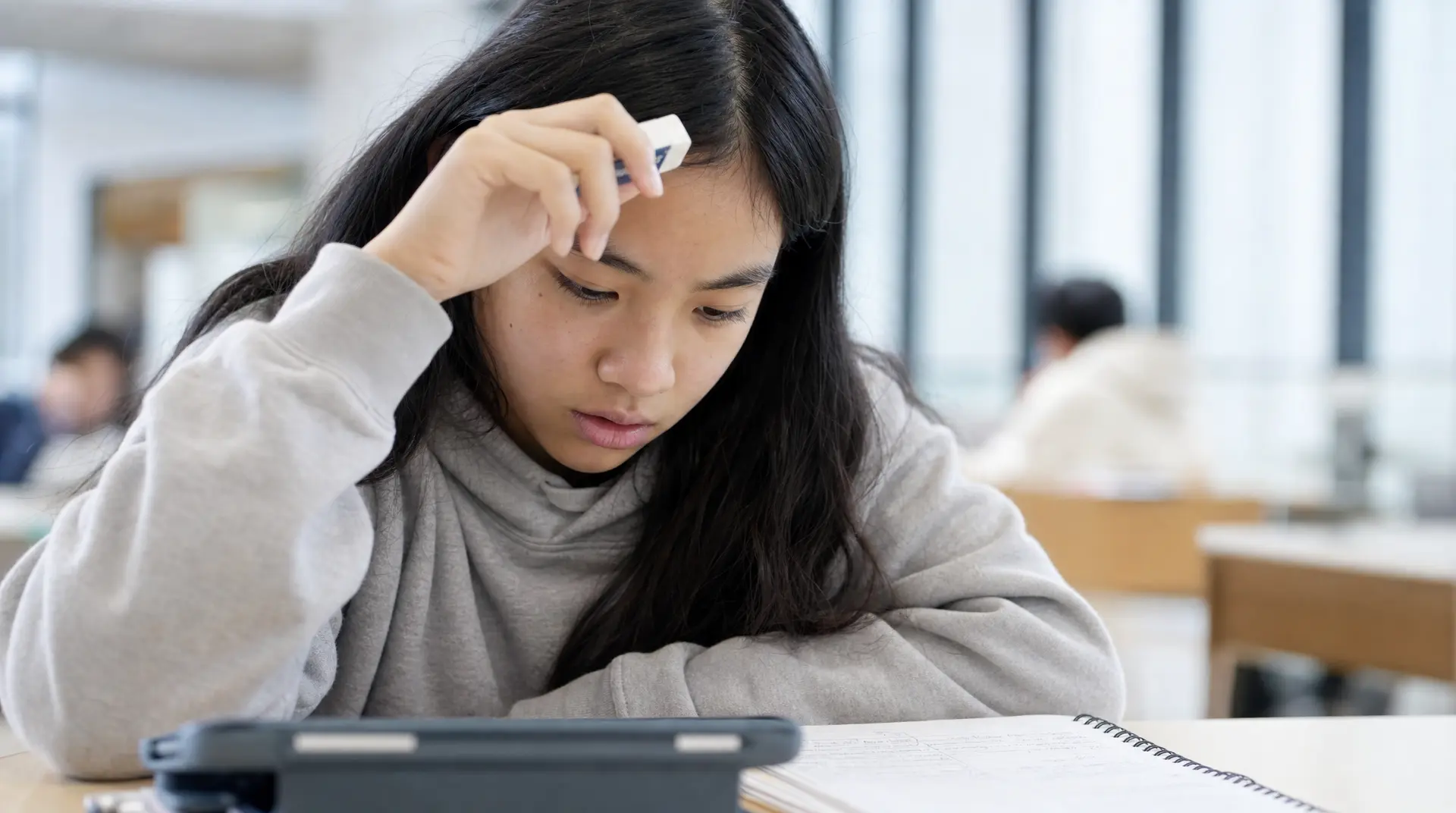 Human Tutor vs AI Homework Help: Why Real Empathy Wins A student sits at a desk with a notebook, resting her forehead in frustration while studying, needing reduce homework stress at home support.